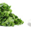a large pile of raw spinach next to a smaller pile of cooked spinach on a white plate.